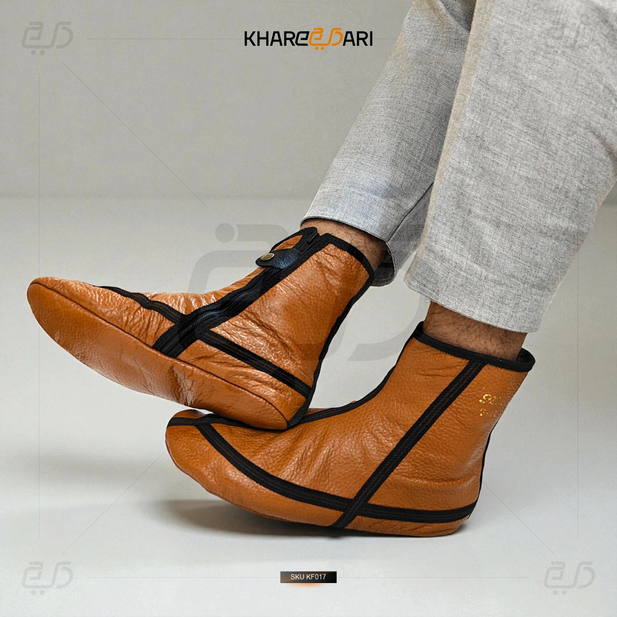 Brown leather shoes with black straps worn by a person in gray pants on a white background. Brown