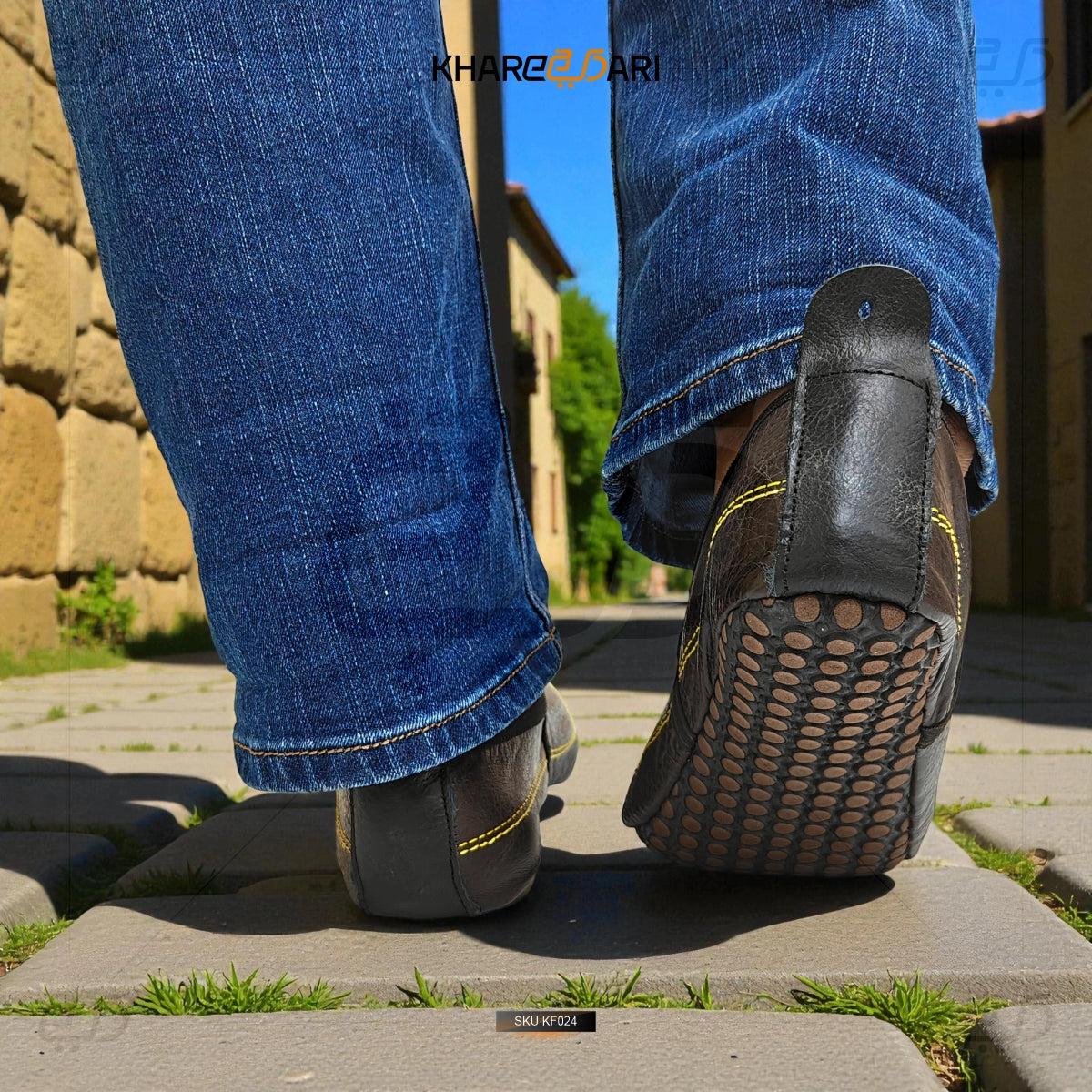 Person wearing blue jeans and black shoes with yellow accents on a stone pavement. Dark Brown