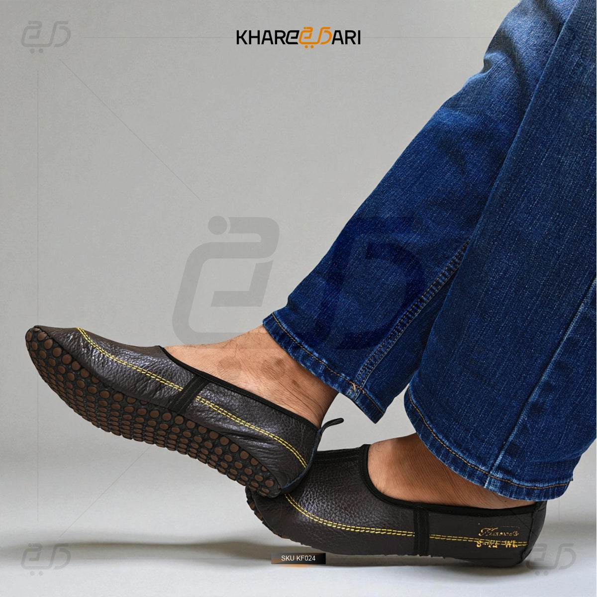 Black leather shoes with yellow stitching worn with blue jeans on a gray background, featuring the brand 'Khareeb Dari'. Dark Brown