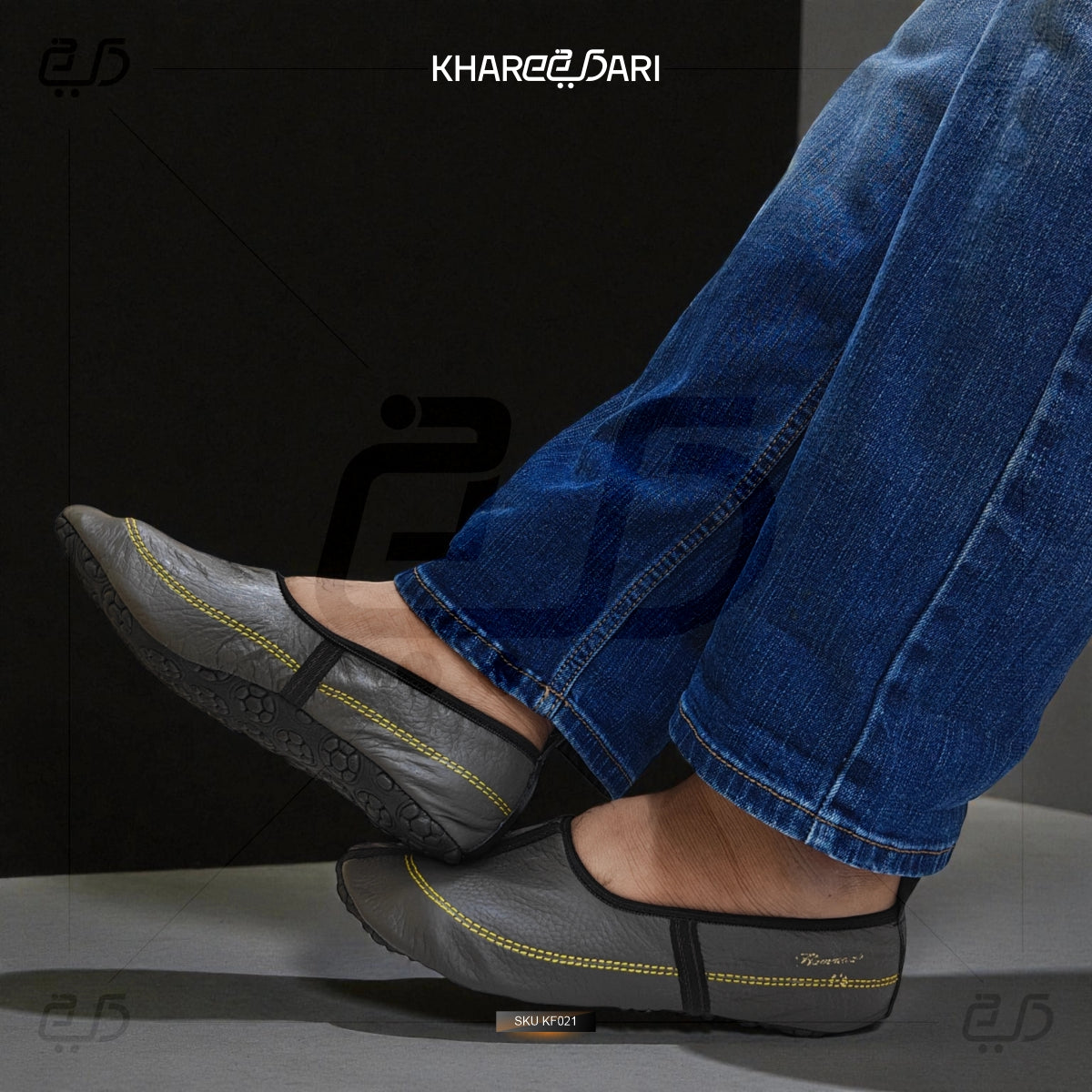 Person wearing gray shoes with yellow stitching and blue jeans, branded 'Khareegiari'. Grey