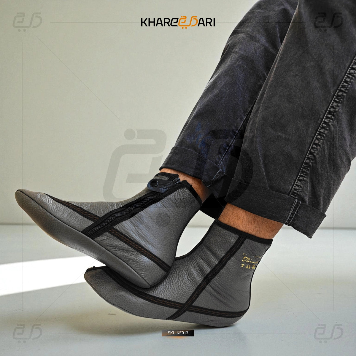 Person wearing gray leather shoes with black straps on a light background, featuring the brand 'Khareeb Dari'. Grey