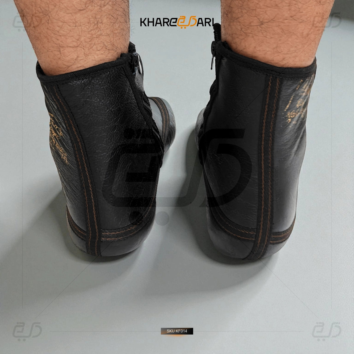 Black leather ankle boots worn by a person on a white background with 'KHAREZDARI' branding. Black