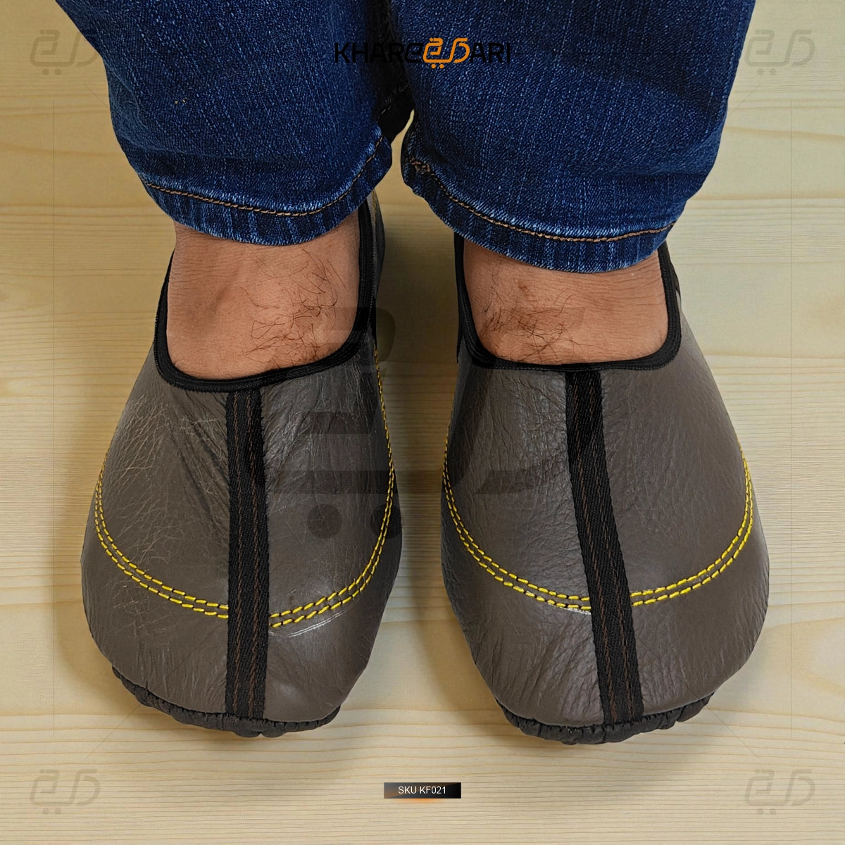 Gray slip-on shoes with yellow stitching worn by a person on a wooden floor. Dark Brown