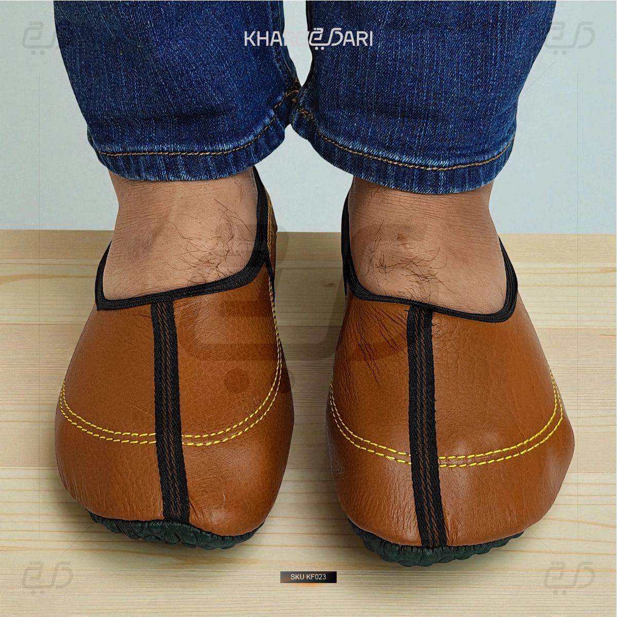 Brown leather shoes with black straps worn by a person in blue jeans on a wooden floor. Brown