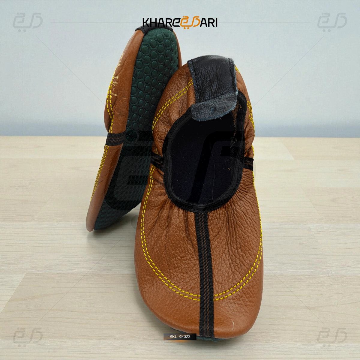 Brown leather slippers with black accents on a light wooden surface, branded 'Khareebari'. Brown